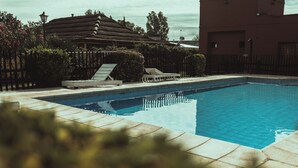 A rectangular swimming pool with a tiled edge, surrounded by a fence and a building with a thatched roof. - Hacienda Altomonte (San Rafael)