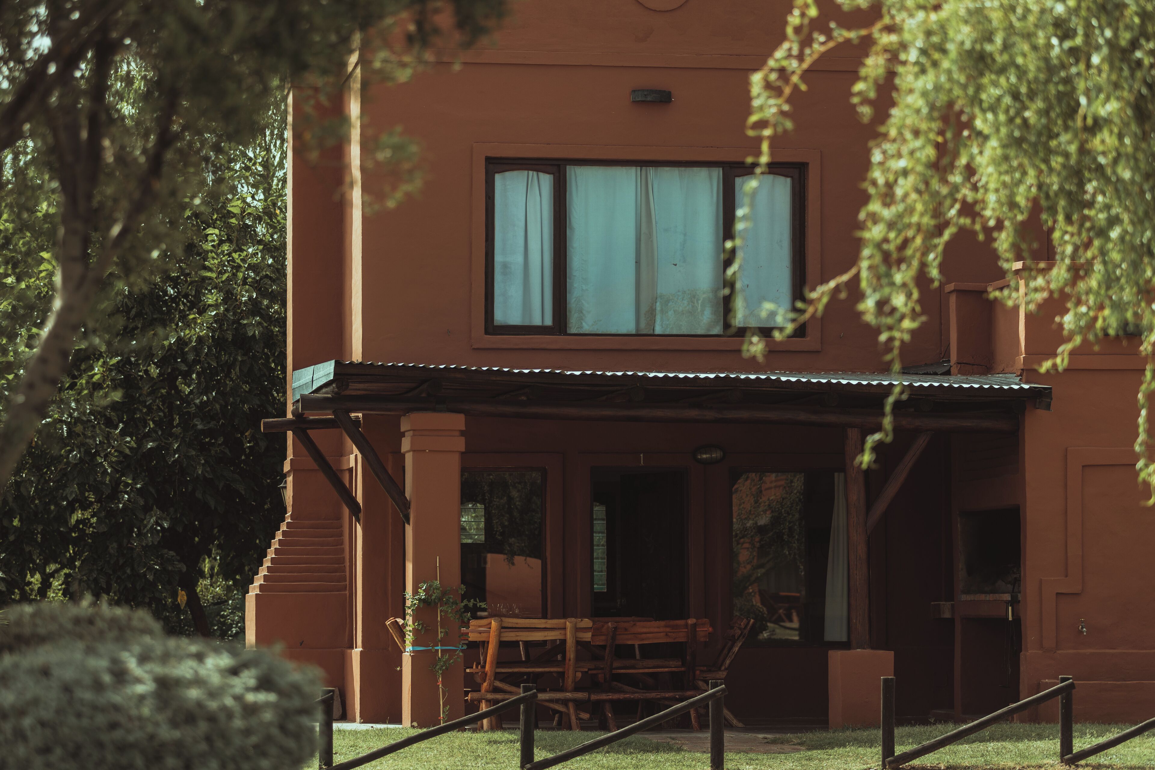 A building with a covered porch, a staircase, and a window with curtains.