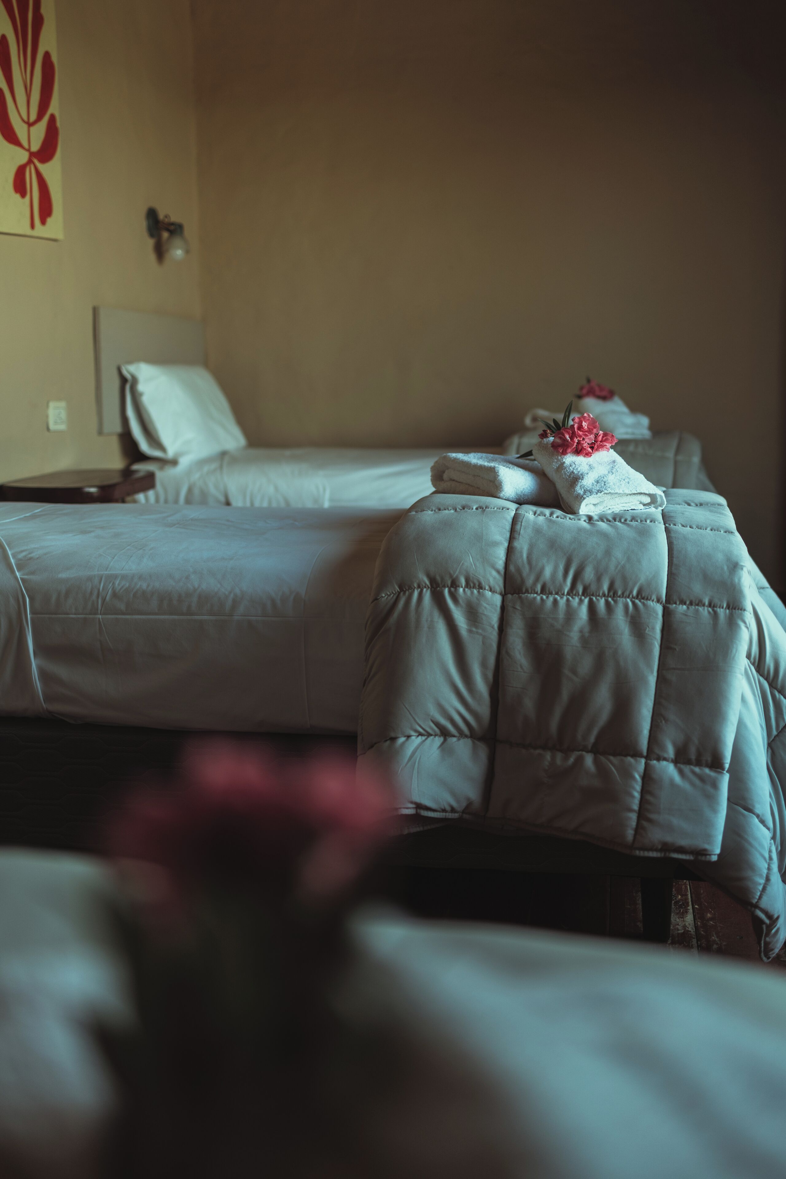 Habitación de hotel con dos camas, cada una con un cabecero acolchado y una toalla doblada con cuidado.