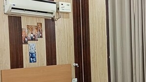 A hotel room with a bed, an air conditioning unit, a ceiling fan, and curtains. - VS Grand (Bara Banki)