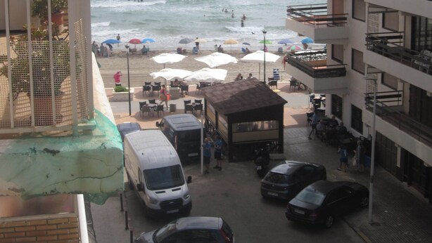 A beachfront hotel with balconies overlooking the sea, outdoor seating, and parked vehicles. - Sunny beach apartment in Las Palmeres/Valencia (Sueca/Les Palmeres)