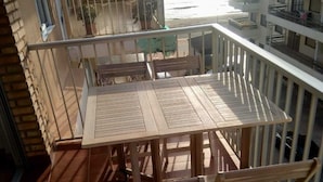 A balcony with a wooden table and chairs, a view of the sea, and a building with balconies in the background. - Sunny beach apartment in Las Palmeres/Valencia (Sueca/Les Palmeres)