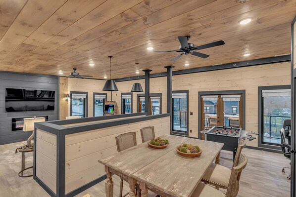 A spacious kitchen with a wooden ceiling, a central island, and a foosball table. - Roof Top Cabin~Water Park~Heater Indoor Pool~Games~PlayStation~Games~Mini-Golf~Views~Sleep 22 (Sevierville)