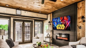 A living room with a Star Wars TV, a fireplace, and a ceiling fan. - Roof Top Cabin~Water Park~Heater Indoor Pool~Games~PlayStation~Games~Mini-Golf~Views~Sleep 22 (Sevierville)