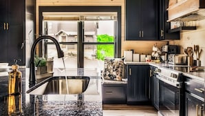 A modern kitchen with dark cabinetry, a granite countertop, and a view through a glass door. - Roof Top Cabin~Water Park~Heater Indoor Pool~Games~PlayStation~Games~Mini-Golf~Views~Sleep 22 (Sevierville)