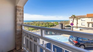 Un balcon donnant sur la mer, une voiture garée dans la rue et un immeuble avec un toit en tuiles.