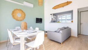 Un espace de vie moderne comprenant un coin repas, un canapé gris, un grand miroir et une étagère en bois.