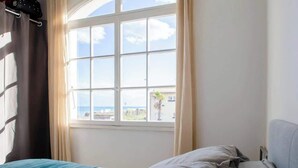 Une chambre avec un lit, une fenêtre avec des rideaux et une vue sur la mer.
