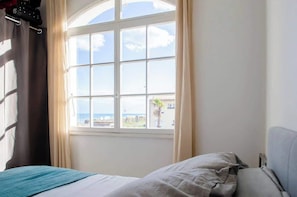 A room with a bed, a window with curtains, and a view of the sea.