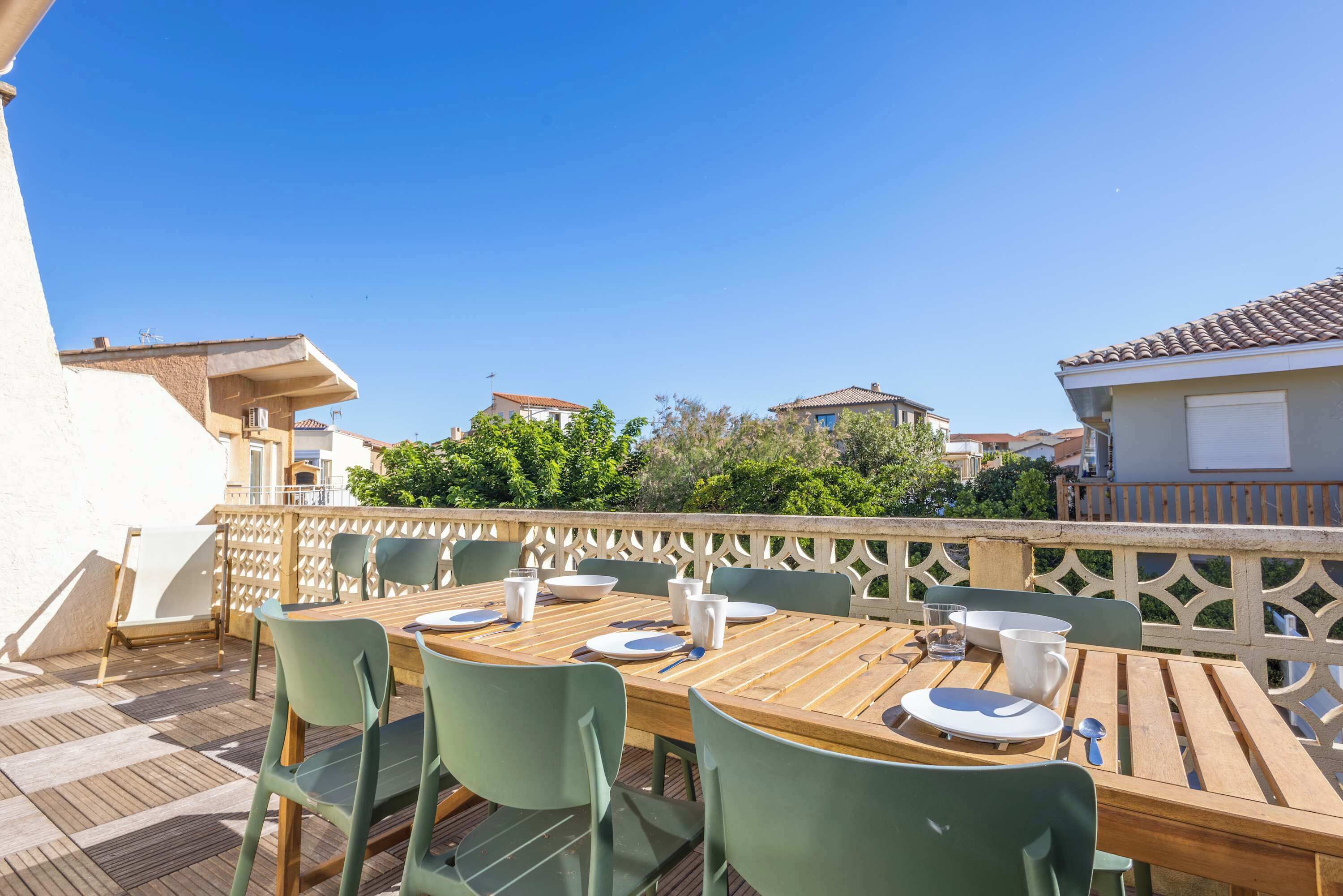 An outdoor dining area with a wooden table, green chairs, and a white fence.