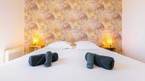 Une chambre d’hôtel avec un papier peint à motifs floraux, deux lampes de chevet, un lit bien fait avec deux serviettes et des oreillers blancs.