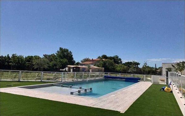 A rectangular swimming pool with a diving board, surrounded by a white fence, and a grassy area.