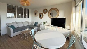 A modern living room with a sofa, TV, dining table, and decorative mirrors.