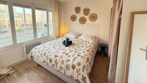 A bedroom with a bed, a bedside table, a lamp, and a window with a view of buildings.