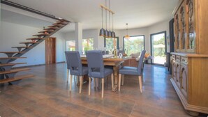 A spacious dining area with a modern staircase, a large wooden cabinet, and a view of the outdoors.