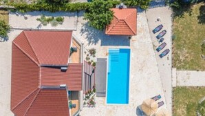 An aerial view of a property with a swimming pool, two red-roofed buildings, and a patio area with umbrellas.