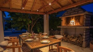 An outdoor dining area with a wooden table and chairs, a fire pit, and a view of trees.