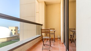 Un balcón con una mesa y sillas, vista de un edificio y suelo de baldosas.