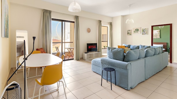 Una sala de estar moderna con un sofá, una mesa de comedor con sillas, un televisor y un balcón con vistas.