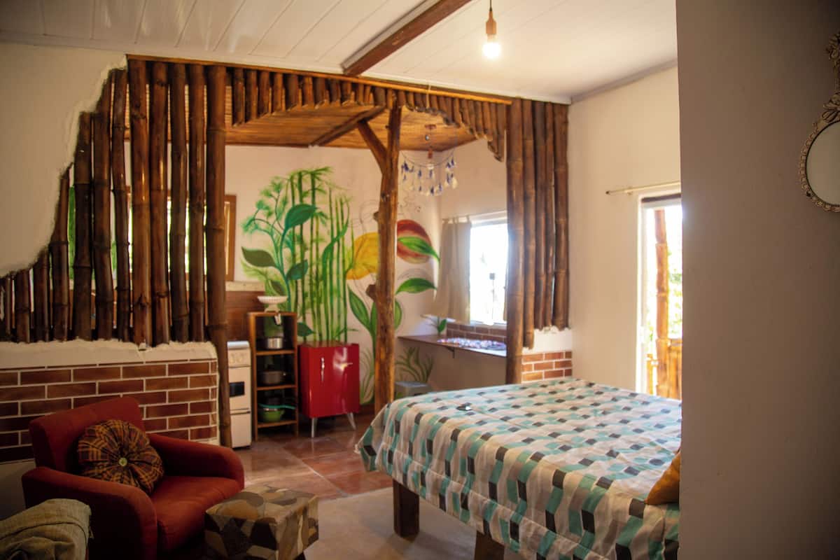 Quarto com uma cama, uma cadeira vermelha, um painel de madeira e um mural de plantas.