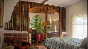 Una habitación con una cama, una silla roja, una mesita, un armario rojo y una partición de bambú.