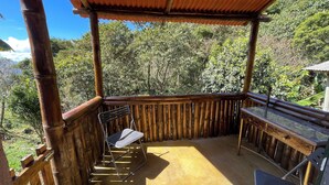 Un espacio exterior techado con barandilla de bambú, una silla de metal y una mesa.