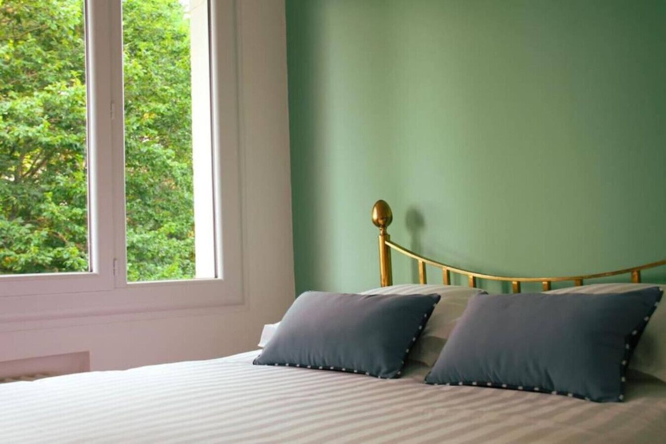 Un dormitorio con cama, dos almohadas, una ventana y una pared verde.