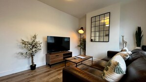 A modern living room with a flat-screen TV, wooden furniture, a coffee table, a sofa, and decorative items including a plant and a mirror. - 3 Bedroom Home in Wellington (Wellington)
