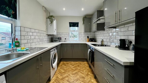A modern kitchen with grey cabinets, a built-in washing machine, and a herringbone wood floor. - 3 Bedroom Home in Wellington (Wellington)