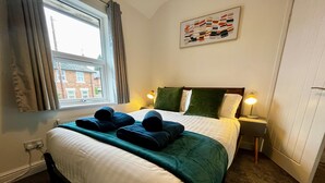 A neatly made bed with a green blanket and two folded towels, a bedside lamp, and a window with curtains. - 3 Bedroom Home in Wellington (Wellington)