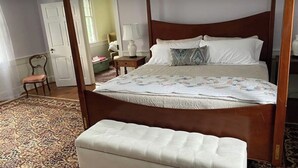 Una cama con dosel con colcha, una mesita de noche con lámpara, una silla y una alfombra estampada.
