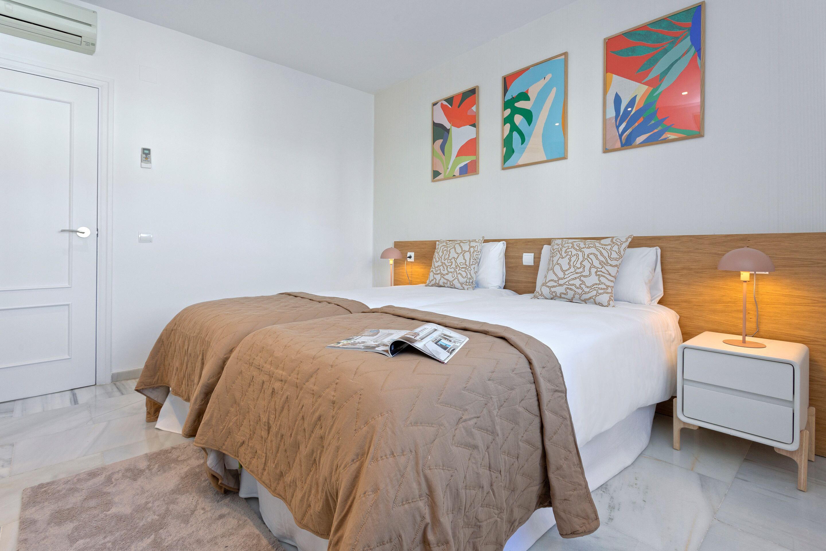A neatly arranged bedroom with a large bed, bedside tables, and colorful abstract wall art.