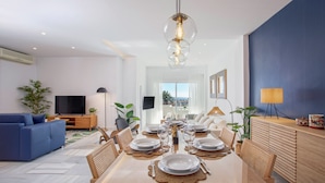 A modern dining area with a glass-top table, surrounded by wooden chairs, and a hanging light fixture. - Genteel Home Royal Gardens Marbella (Marbella)