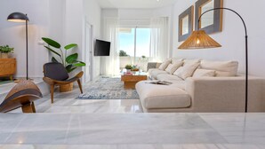 A modern living room with a sofa, armchairs, a coffee table, a TV, and a large window with curtains. - Genteel Home Royal Gardens Marbella (Marbella)