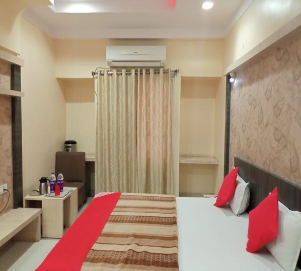 A hotel room with a bed, a nightstand, a desk, an air conditioning unit, and a curtain.
