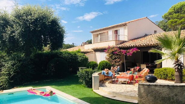 A poolside area with a pool, lounge chairs, and a house with a tiled roof.
