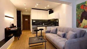A modern living room with a grey sofa, a black coffee table, and a kitchen area with white cabinets and black countertops.