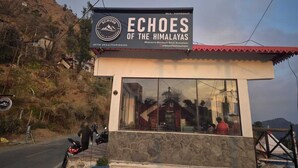 A building named 'Echoes of the Himalayas' with a signboard, a stone facade, and a view of the surrounding landscape. - Echoes of the Himalayas (Suwakholi)