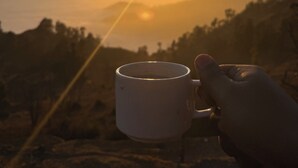 A hand holding a mug with a sunset in the background. - Echoes of the Himalayas (Suwakholi)