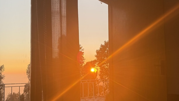 An open doorway leading to a balcony with a view of the sunset. - Echoes of the Himalayas (Suwakholi)
