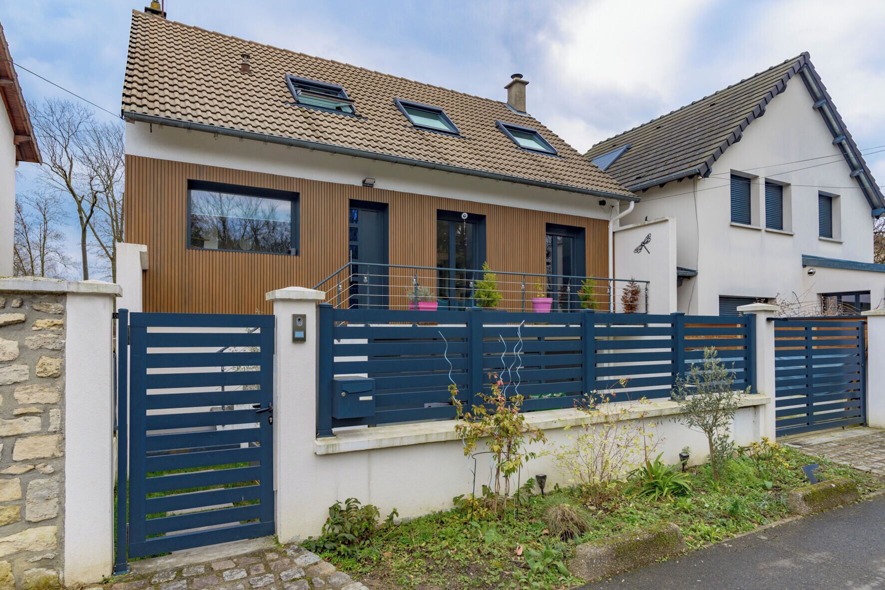 Een modern huis met twee verdiepingen, een pannendak, een houten gevel en een blauwe poort.