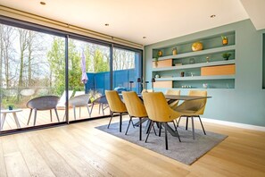 A modern dining area with a large glass door leading to an outdoor patio, a round table, and several chairs. - Paris Garden River residence (Creteil)
