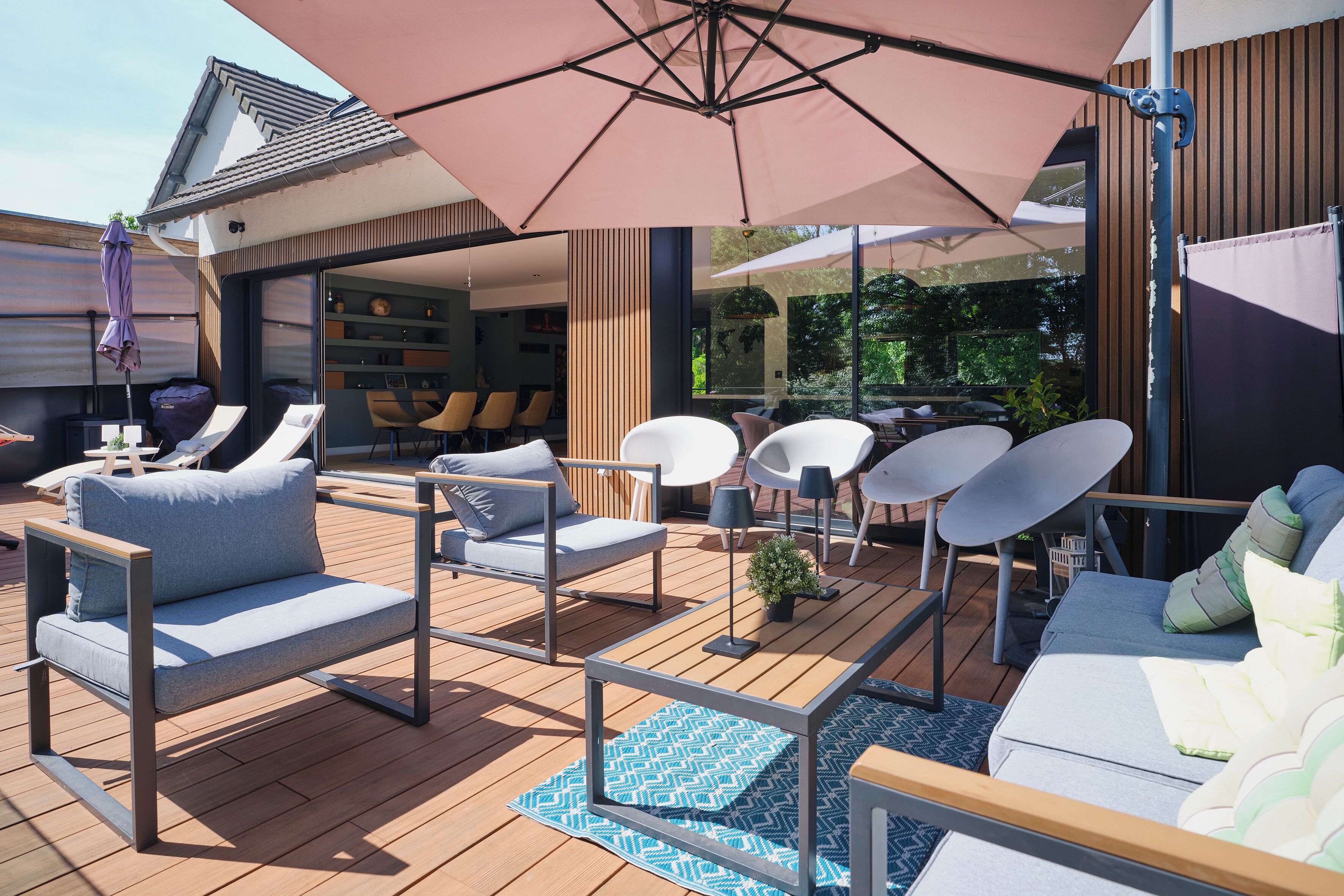 Terraza exterior con mobiliario moderno, incluyendo un sofá y sillones, bajo grandes sombrillas.