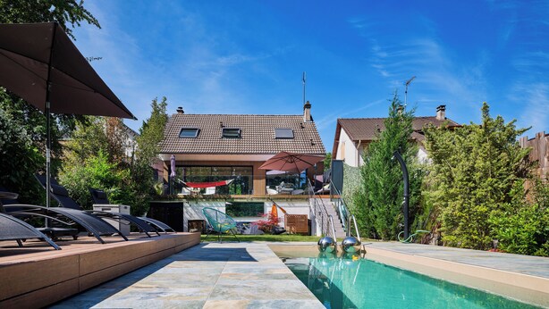 Un área de piscina con sillones de descanso, un jacuzzi y vista a una casa al fondo.