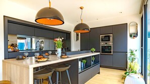 Una cocina moderna con una isla central, taburetes de bar, iluminación colgante y electrodomésticos integrados.