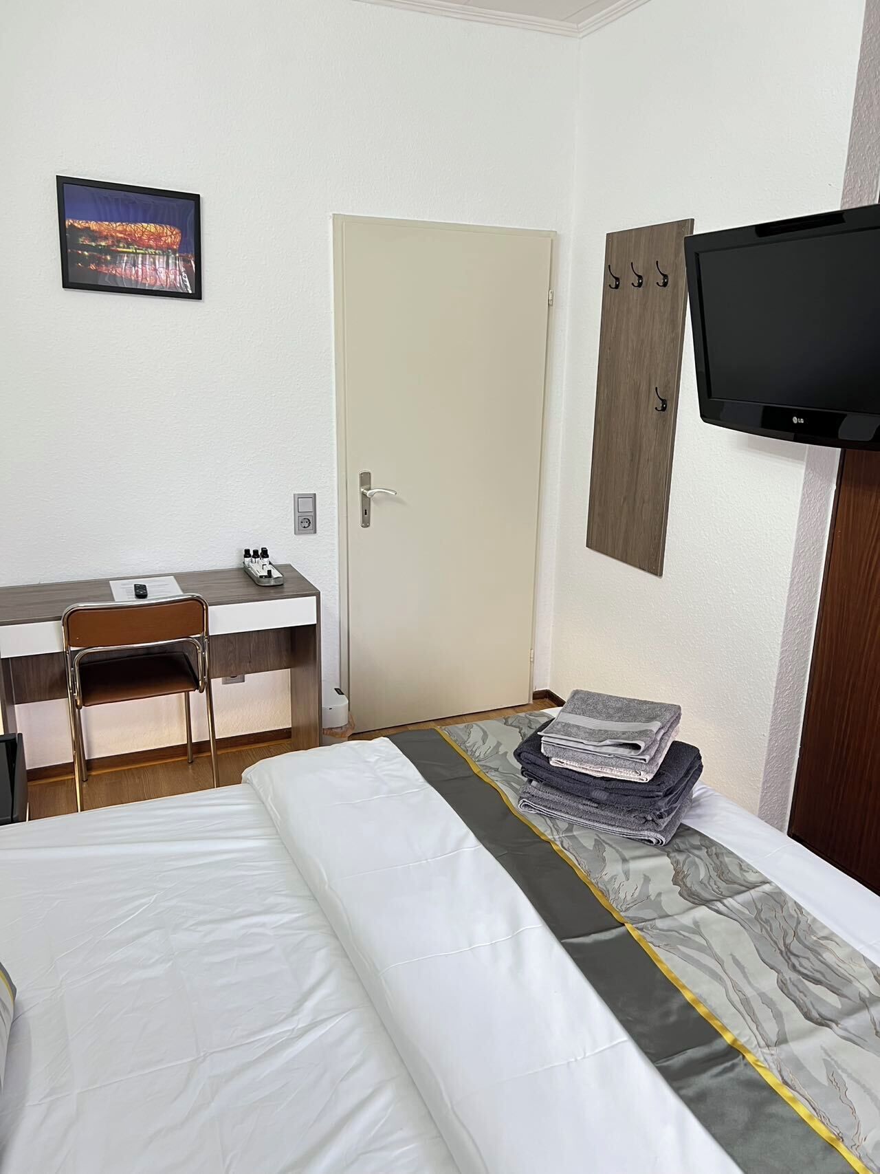 A hotel room with a bed, a desk, a chair, a television, and a door.
