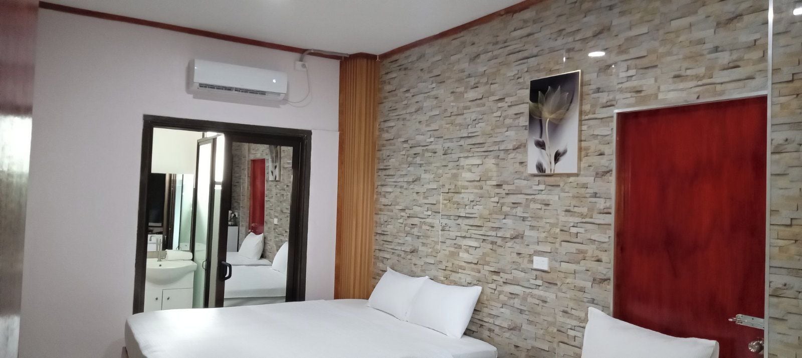 A hotel room with a bed, a red door, a stone wall, and a picture of flowers.