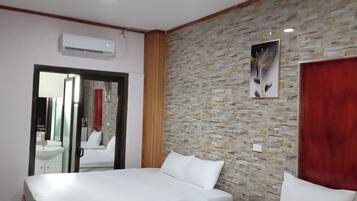 A hotel room with a bed, a red door, a stone wall, and a picture of flowers.