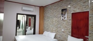 Una camera d'albergo con un letto, una porta rossa, un muro in pietra e un quadro con fiori.