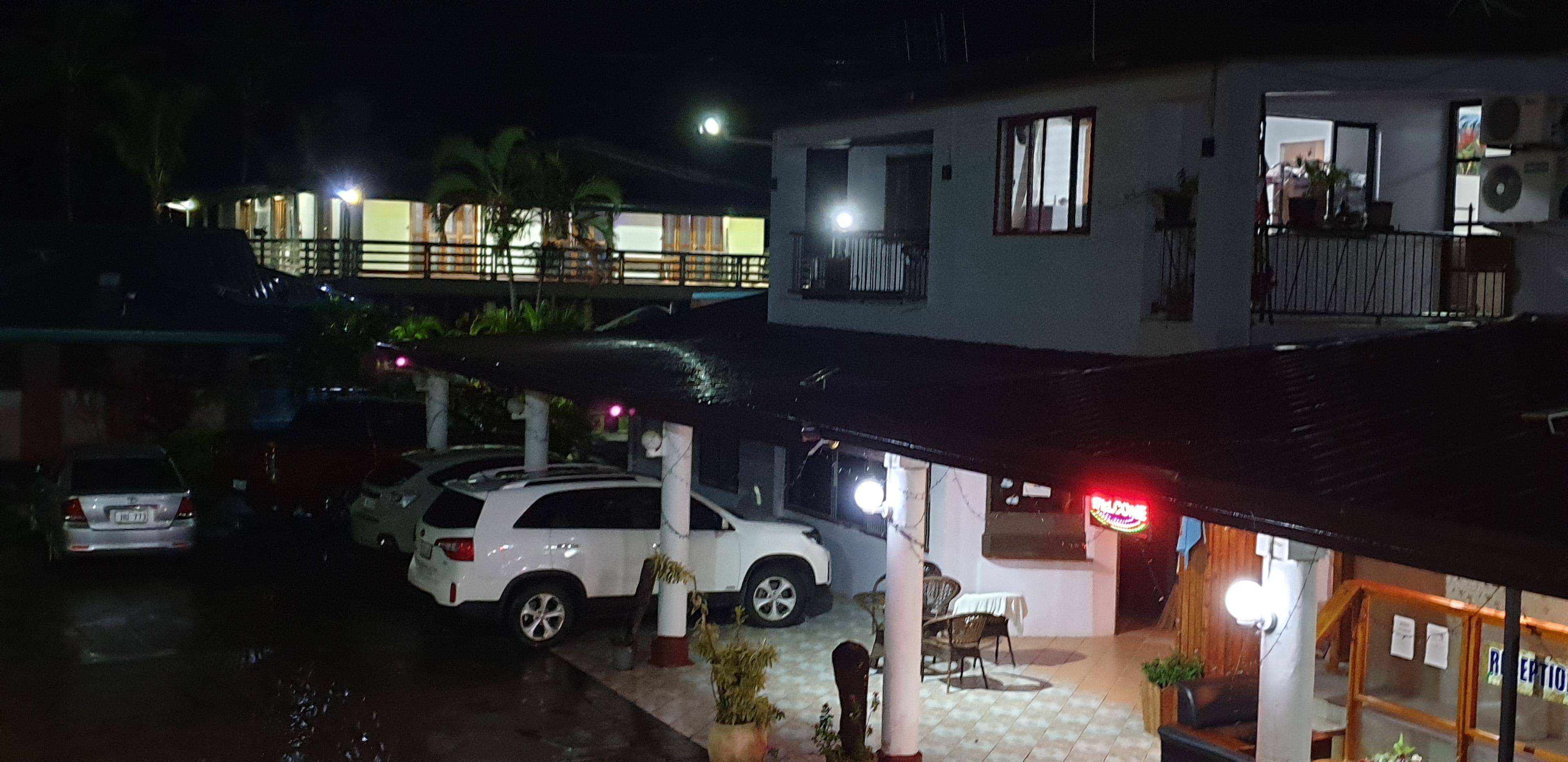 Edificio de dos pisos con un automóvil estacionado adelante, un balcón en el nivel superior y un letrero que dice 'RECEPTION'.
